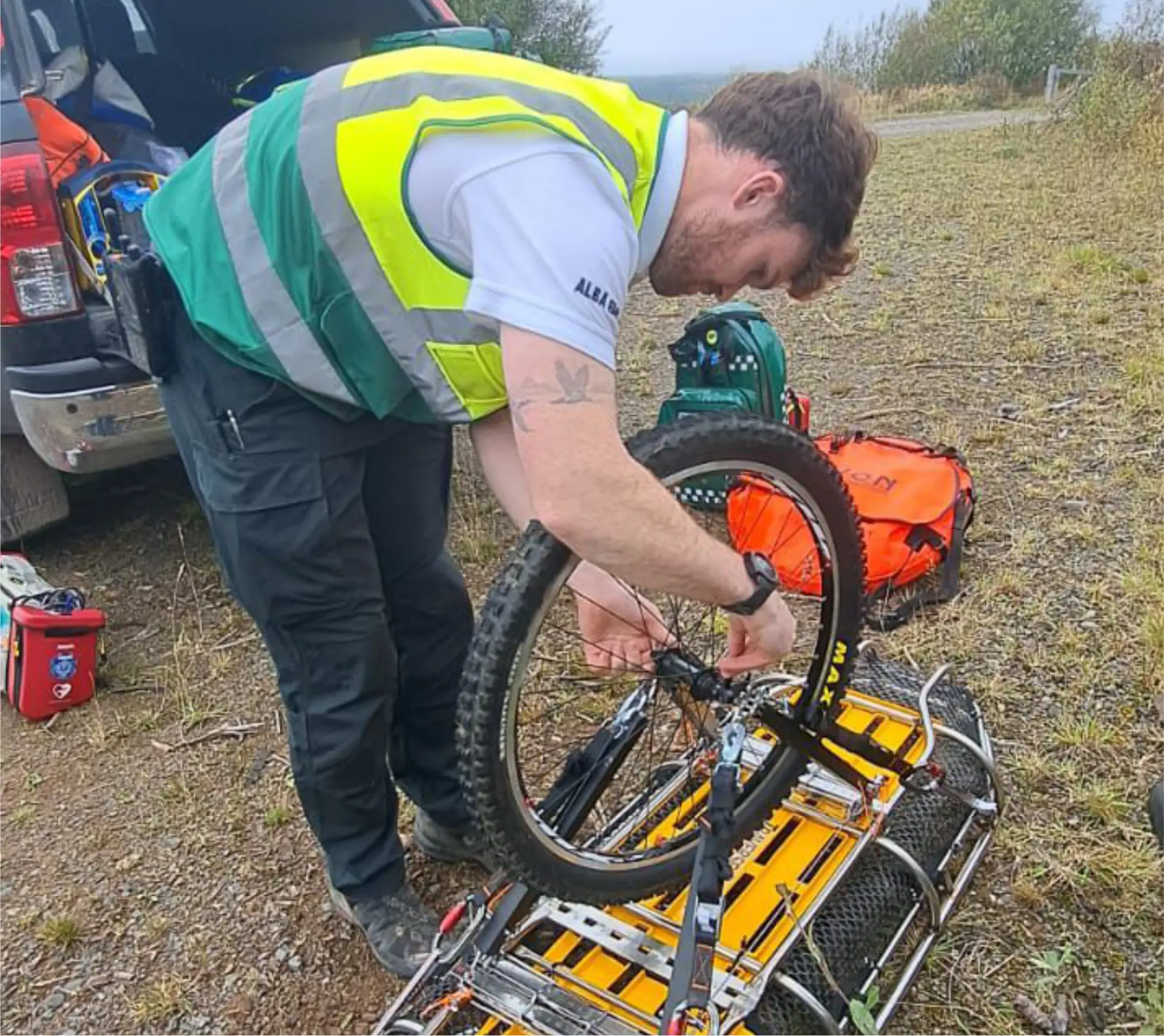 Alba EMS clinician preparing an off-road wheeled stretcher beside a response vehicle in open countryside