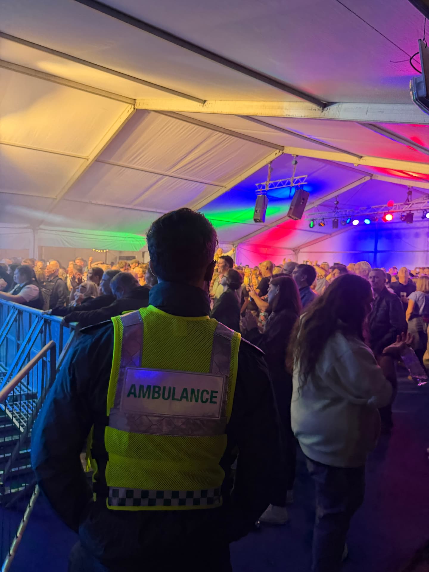 Alba EMS responder in an ambulance vest watching over a busy, colourfully lit festival tent crowd